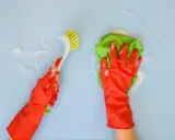 Ręce w czerwonych rękawiczkach czyszczą niebieską powierzchnię. Jedna ręka trzyma szczotkę, druga zieloną ściereczkę. Użyj odtłuszczacza do ścian, by pozbyć się brudu.