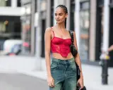 Frau mit geflochtenen conros Haare trägt ein rotes Korsett-Top und Jeans.
