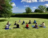 Grupp med människor på en grön gräsmatta under en yoga retreat. En instruktör sitter framför gruppen.