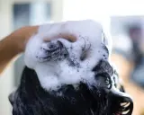 Mano che massaggia shampoo schiumoso sui capelli scuri, puliti o sporchi, per un momento di relax.