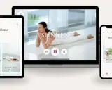 En kvinna utför morgon yoga på en matta. Skärmar visar yogaövningar och pass.