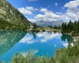 Lago alpino cristallino, perfetto per passeggiate in montagna Lombardia. Riflessi di cielo e montagne.