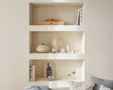 Una nicchia nel muro del salotto, con libri, vasi e diffusore, crea un angolo accogliente e ordinato.