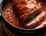 Un succulento polpettone al forno, affogato in un sugo rosso intenso, con una fetta tagliata che rivela un cuore filante di formaggio.