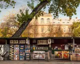 Ein Stand auf dem **Flohmarkt Paris** mit Postkarten, Büchern und Gemälden vor einem historischen Gebäude.