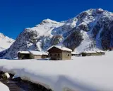 Case innevate nel Val di Rezzalo, con baite in pietra e legno. Per sapere val di rezzalo come arrivare, segui il ruscello che scorre tra la neve.