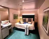 Interno di una royal caribbean cabine con letto matrimoniale, specchio, scrivania e valigia pronta per il viaggio.
