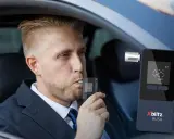 Mężczyzna w garniturze dmucha w alkomat w samochodzie.