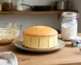 Un délicieux gâteau au yaourt, prêt à être décoré. À côté, un bol de crème, un pot de yaourt et de la farine.