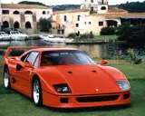 Roter Ferrari F40 auf einer Wiese, im Hintergrund ein Hafen mit Booten und Häusern. Der Ferrari F40 Neupreis war damals ein Traum.