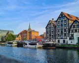 Bydgoszcz atrakcje: rzeka Brda, łodzie, zabytkowa kamienica z postacią na linie i nowoczesny budynek.