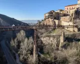 Puentes de Cuenca: una estructura de hierro cruza un barranco, con casas colgando de acantilados rocosos al fondo.