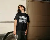 Joven con gafas de sol naranjas y camiseta negra con el diseño "BRANDON MONTOYA NO ES COMO YO".