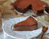 Un trozo de pastel de chocolate cubierto de cacao en polvo, con el pastel entero al fondo.