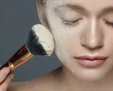 Applicazione di cipria per il baking trucco su un viso, con un pennello carico di prodotto.