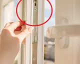 Dłoń reguluje okucia okna plastikowego, by je uszczelnić i zapobiec przewiewom.