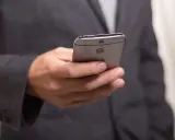 Mężczyzna w garniturze trzyma telefon, być może otrzymuje wiadomość o zawieszeniu działalności.