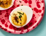 Deviled eggs deutsch: halbe hartgekochte Eier mit cremiger Füllung, bestreut mit Schnittlauch und Gewürzen, auf einem pinkfarbenen Teller mit roten Tupfen.