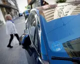 Una mujer cruza la calle mientras un coche eléctrico, con distintivo DGT, espera. Los coches eléctricos pagan zona azul.