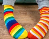 Kolorowe skarpetki w paski, tęczowe i pomarańczowo-białe, leżą na drewnianej podłodze. Jak doprać kolorowe skarpetki?
