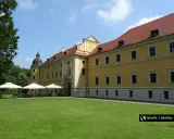 Żółty pałac z czerwonym dachem, gdzie można usiąść pod parasolami. W oddali widać drzewa, a na trawniku rozłożono stoliki. To miejsce, gdzie można poczuć atmosferę rudy raciborskie.