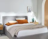 Cama gris con cojines naranjas y beige, perfecta para organizar canapé y crear un ambiente acogedor.