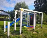 Plac zabaw w **dolinie roztoczy**: zjeżdżalnia, drabinki, huśtawka i ścianka wspinaczkowa. W tle altana.