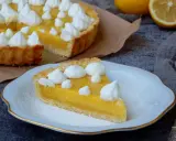 Une part de tarte au citron, garnie de meringue, sur une assiette. La tarte entière est visible en arrière-plan. Une recette de tarte au citron parfaite pour le dessert.