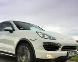 Biały Porsche Cayenne 2025 pędzi po drodze, chmury na niebie sugerują dynamiczną podróż.