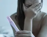Dziewczyna z zakrytą twarzą trzyma test ciążowy, przeżywając strach przed ciążą po stosunku.