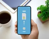 Dłoń trzyma smartfon z ekranem pokazującym proces aktywacji eSIM. Obok kubek kawy i roślinka.