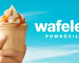 Lody McDonald's w wafelku z polewą karmelową, trzymane w dłoni na tle błękitnego nieba.