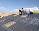 Zwei Handwerker sanieren ein Eternitdach. Die Kosten für die Sanierung eines Eternitdachs sind oft eine wichtige Überlegung.