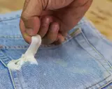 Mano quitando chicle pegado en un bolsillo de jeans. Aprende cómo quitar chicle de la ropa fácilmente.