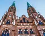 Dwie wieże ceglanego kościoła z zielonymi iglicami, jeden z najpiękniejszych kościołów w Polsce, pod błękitnym niebem.