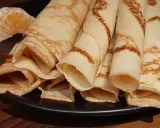 Crêpes à la bière roulées, dorées et légères, servies sur une assiette noire avec un quartier d'orange. Un délice !