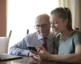Starszy pan i opiekunka patrzą na telefon, dyskutując o tym, ile zarabia opiekunka osób starszych na godzinę.