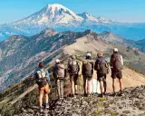 Sześcioro turystów z plecakami na grani, podziwiających majestatyczny szczyt góry na tle błękitnego nieba. To piękny widok z Pacific Crest Trail.