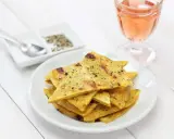 Une assiette de socca à la poêle, coupée en triangles et saupoudrée de poivre, à côté d'un verre de rosé.