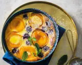 Clafoutis abricot sans gluten, doré et saupoudré de sucre glace, garni de fruits frais et de feuilles de menthe.