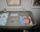 Śpiące dziecko w wózku dla dziecka Singapore Airlines podczas lotu. Wygodny enter air wózek dla dziecka zapewnia spokojny sen maluchowi.