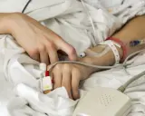 Ręka pacjenta w szpitalnym łóżku, podłączona do aparatury medycznej. Denga to choroba, a tu widzimy jej skutki.
