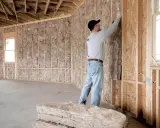 Obrero instala aislamiento en pared de madera. Aprende como aislar una pared para mejorar la eficiencia energética.