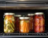 Gläser mit eingelegtem Gemüse, wie Gurken und Karotten, stehen im Ofen. Dies sind leckere Hauptgerichte zum Einkochen, die nach Rezepten zubereitet werden.