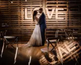 Para nietypowe sesje ślubne, para młoda pozuje przed podświetlanym napisem "LOVE" na tle drewnianych palet.