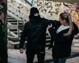 Kobieta używa gazu pieprzowego przeciwko napastnikowi w kominiarce. To przykład obrony koniecznej w niebezpiecznej scenerii z graffiti.