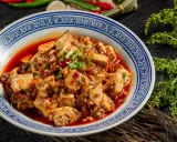Pikantne tofu w sosie chili, klasyka kuchni syczuańskiej. Danie wygląda apetycznie, ozdobione szczypiorkiem.