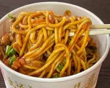 Un tazón lleno de fideos chinos salteados con verduras y salsa. Palillos levantan un bocado.