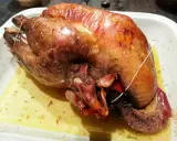 Une pintade au four, dorée et juteuse, repose dans un plat blanc, baignant dans son jus savoureux.