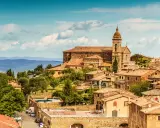 Panoramica del centro storico di Montalcino, con la chiesa e le case in pietra sotto un cielo azzurro con nuvole.